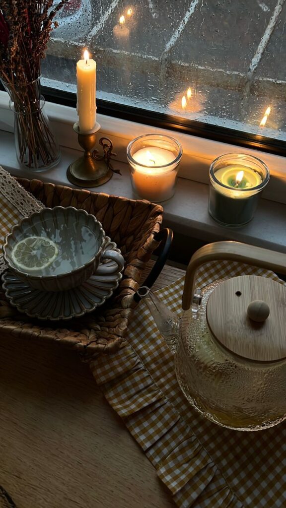 Warm indoor scene with candles, tea, and a rainy window, perfect for relaxing moments.